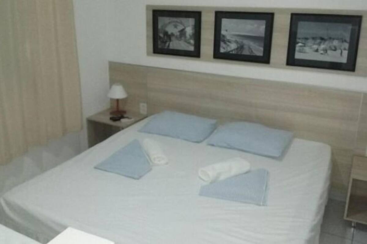 A neatly made bed with pillows and a folded towel, a bedside lamp, and three framed pictures on the wall.
