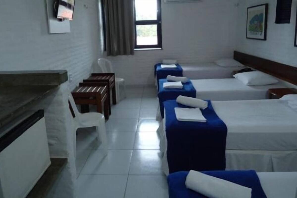 A hotel room with four single beds, a desk, a chair, and a window with curtains.