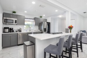 A modern kitchen with grey cabinets, stainless steel appliances, and a central island with bar stools. - Beautiful Vacation Home in Melbourne (Melbourne)