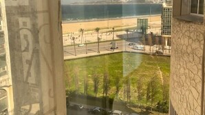 A view from a window overlooking a beach with a parking area and a road in the foreground.