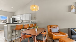 Una cocina moderna con armarios blancos, un comedor con sillas de madera y una lámpara colgante.