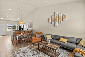 A modern living room with a grey sofa, wooden coffee table, and a dining area with a table and chairs.