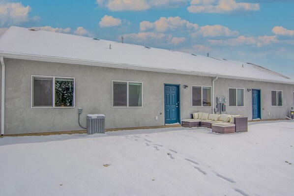 A single-story house with a snow-covered roof and a covered patio area with a sofa and cushions.
