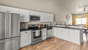 Una cocina moderna con electrodomésticos de acero inoxidable, armarios blancos y piso de madera.