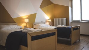 Habitació d'hotel amb dos llits individuals, un radiador i una finestra amb llum natural.