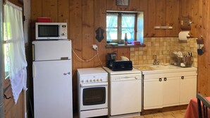 Cozinha compacta com paredes de madeira, uma janela, micro-ondas, frigorífico, fogão e máquina de lavar loiça.