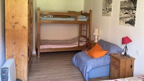 Quarto com beliche, guarda-roupa de madeira, mesa de cabeceira com abajur e um pequeno armário.