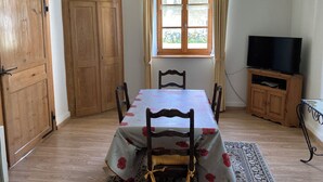 Uma área de refeições com uma mesa posta para quatro pessoas, armários de madeira, uma televisão em um móvel e uma janela com cortinas.