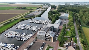 Luchtbeeld van een jachthaven met veel liggende boten, een groot gebouw met schuin dak en een weg ernaast.
