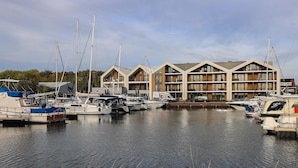 Een jachthaven met verschillende boten die aanmeren, en een modern gebouw met meerdere balkons en grote ramen.