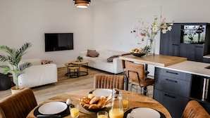 Een moderne woonkamer met een bank, een ontbijt tafel gedekt en een keuken met kasten en een televisie.
