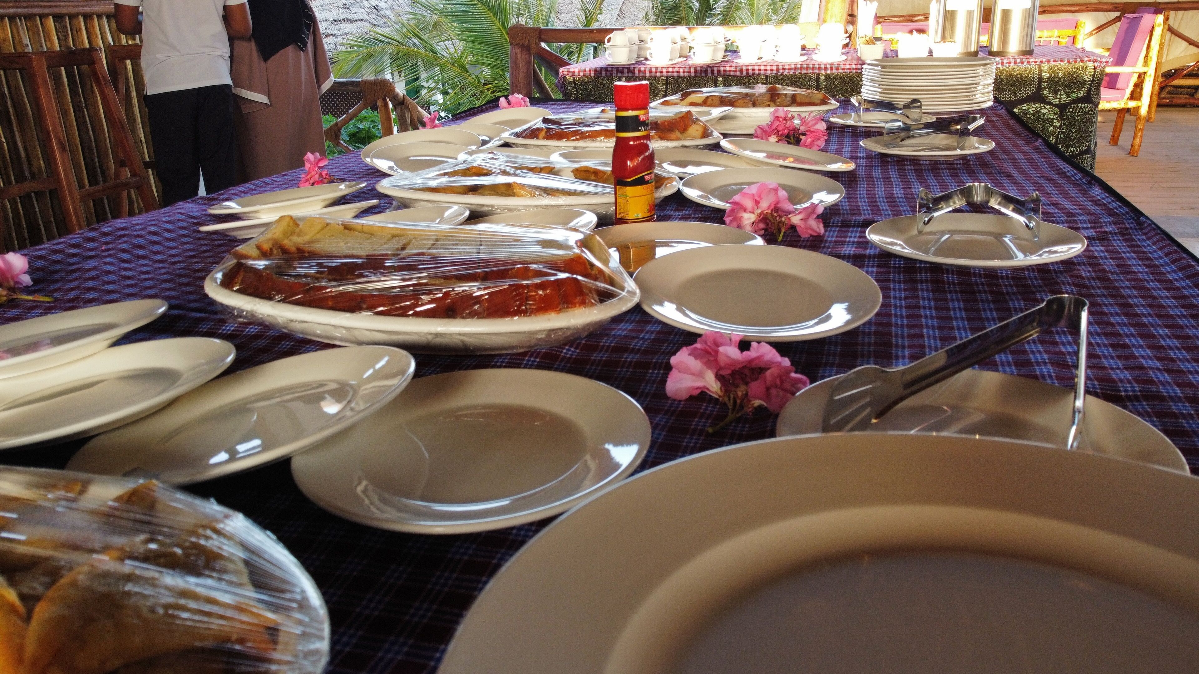 A buffet table with various dishes and utensils, covered with a checkered tablecloth.