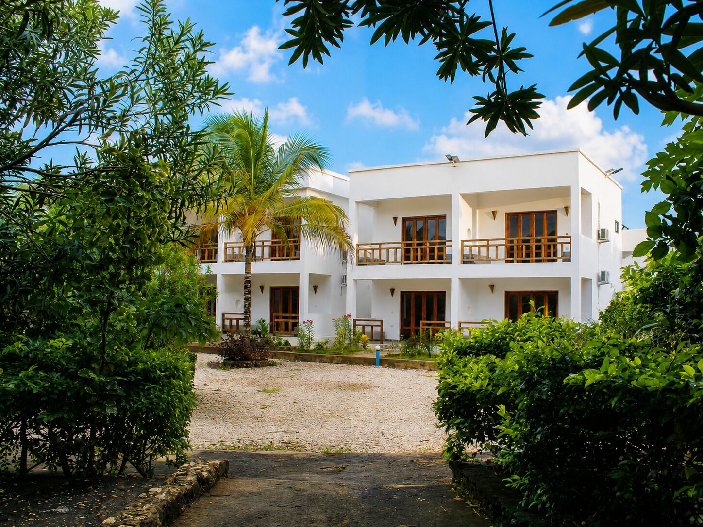 A multi-story building with balconies, surrounded by greenery and a gravel path.