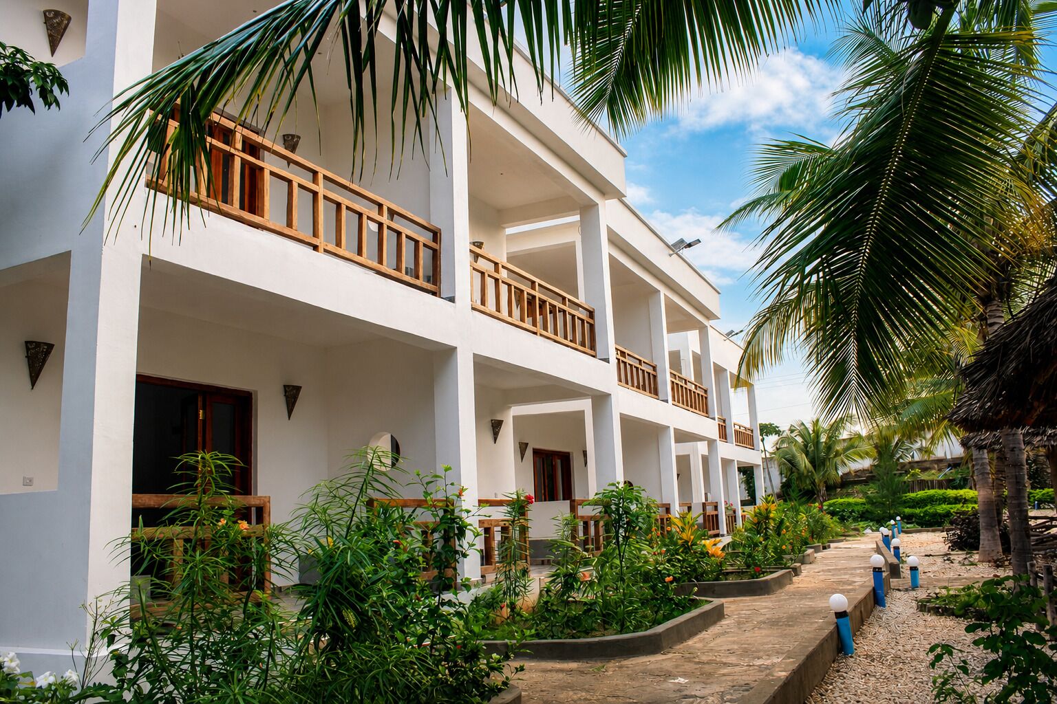Un hotel de varios pisos con balcones, rodeado de exuberante vegetación y palmeras.