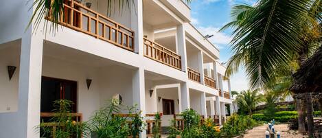Un hotel de varios pisos con balcones, rodeado de exuberante vegetación y palmeras.