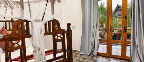 Una habitación con una cama de madera, una ventana con cortinas y vistas a palmeras.