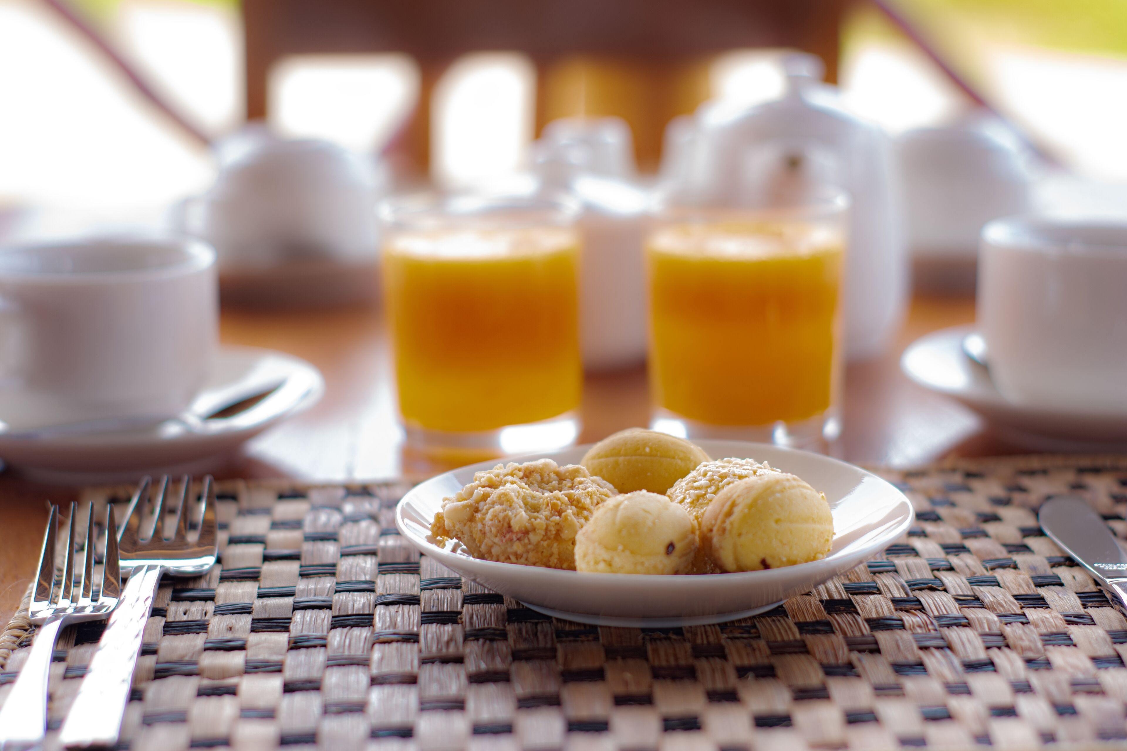 Un desayuno con un plato de pasteles, dos vasos de zumo de naranja y un tenedor y cuchillo sobre un mantel tejido.