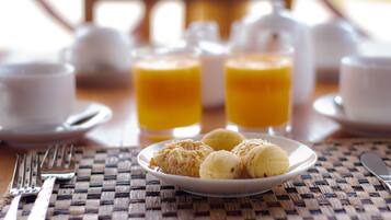 Ein Frühstückstisch mit einer Auswahl an Gebäck, zwei Gläsern Orangensaft sowie Gabel und Messer auf einer gewebten Tischmatte.