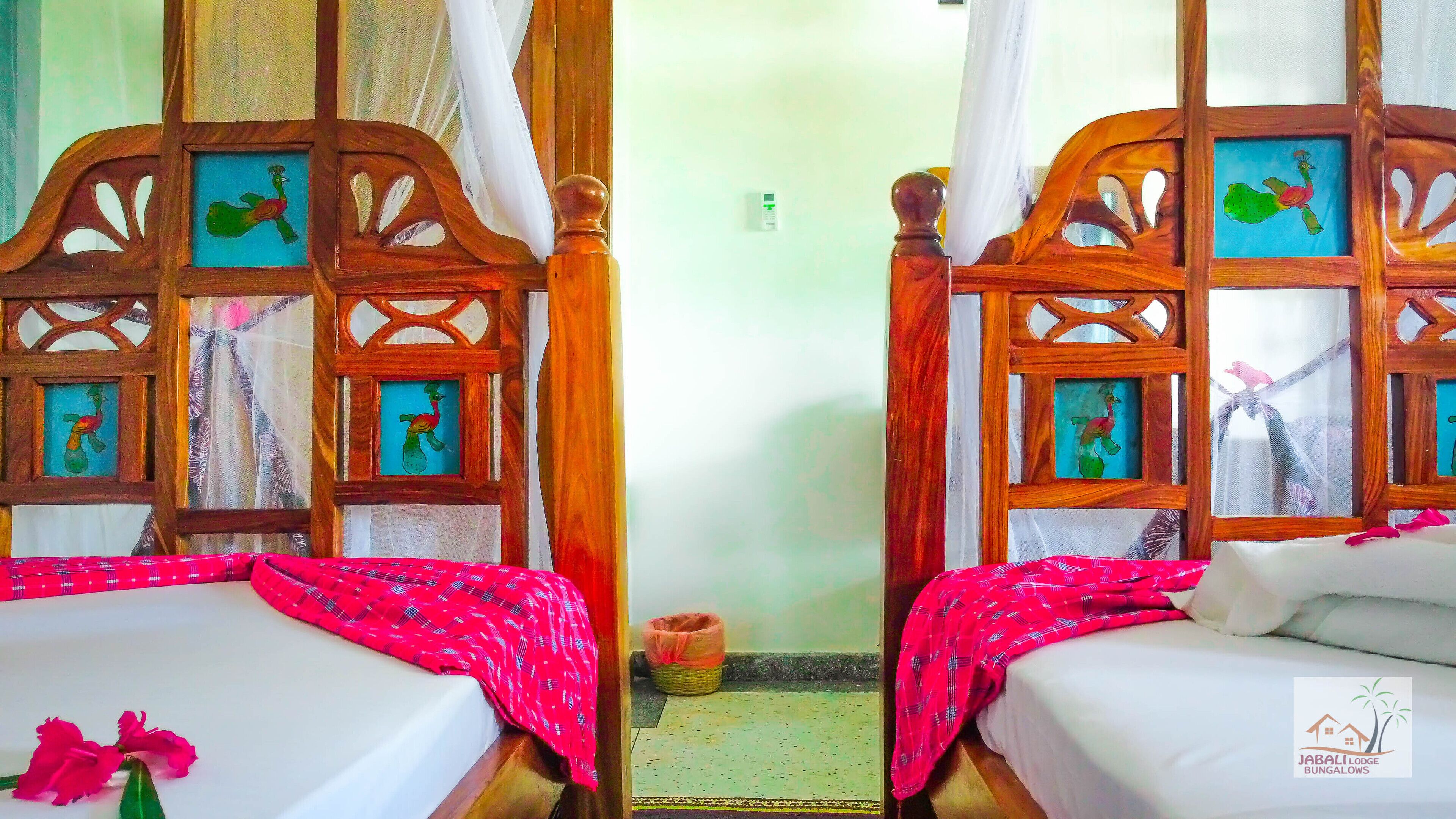 A room with two wooden beds, each with a framed picture of a peacock.