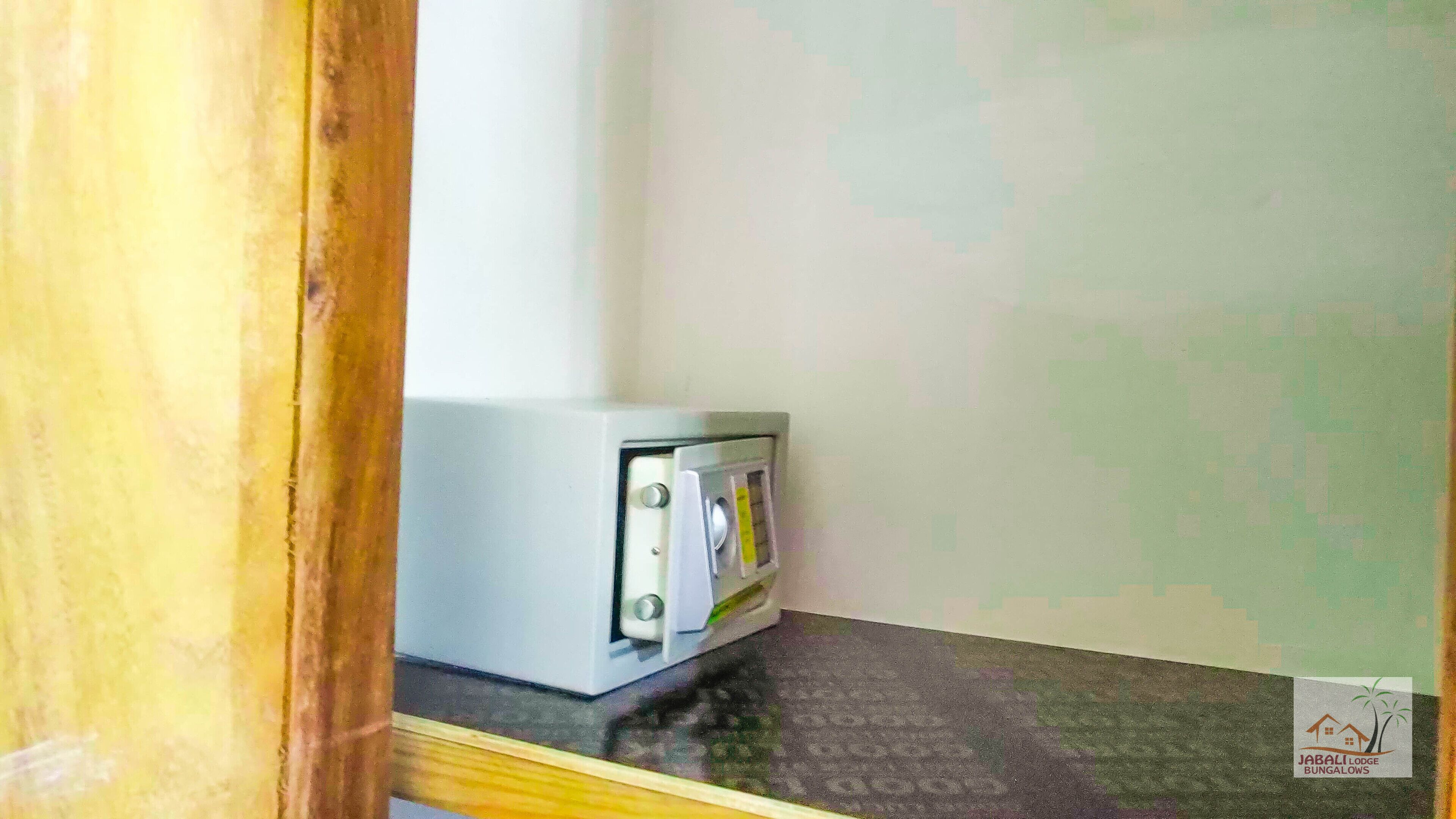 Quarto com pequena área de cozinha compacta, moldura de porta de madeira e logotipo de 'JABALI LODGE BUNGALOWS' na parede.