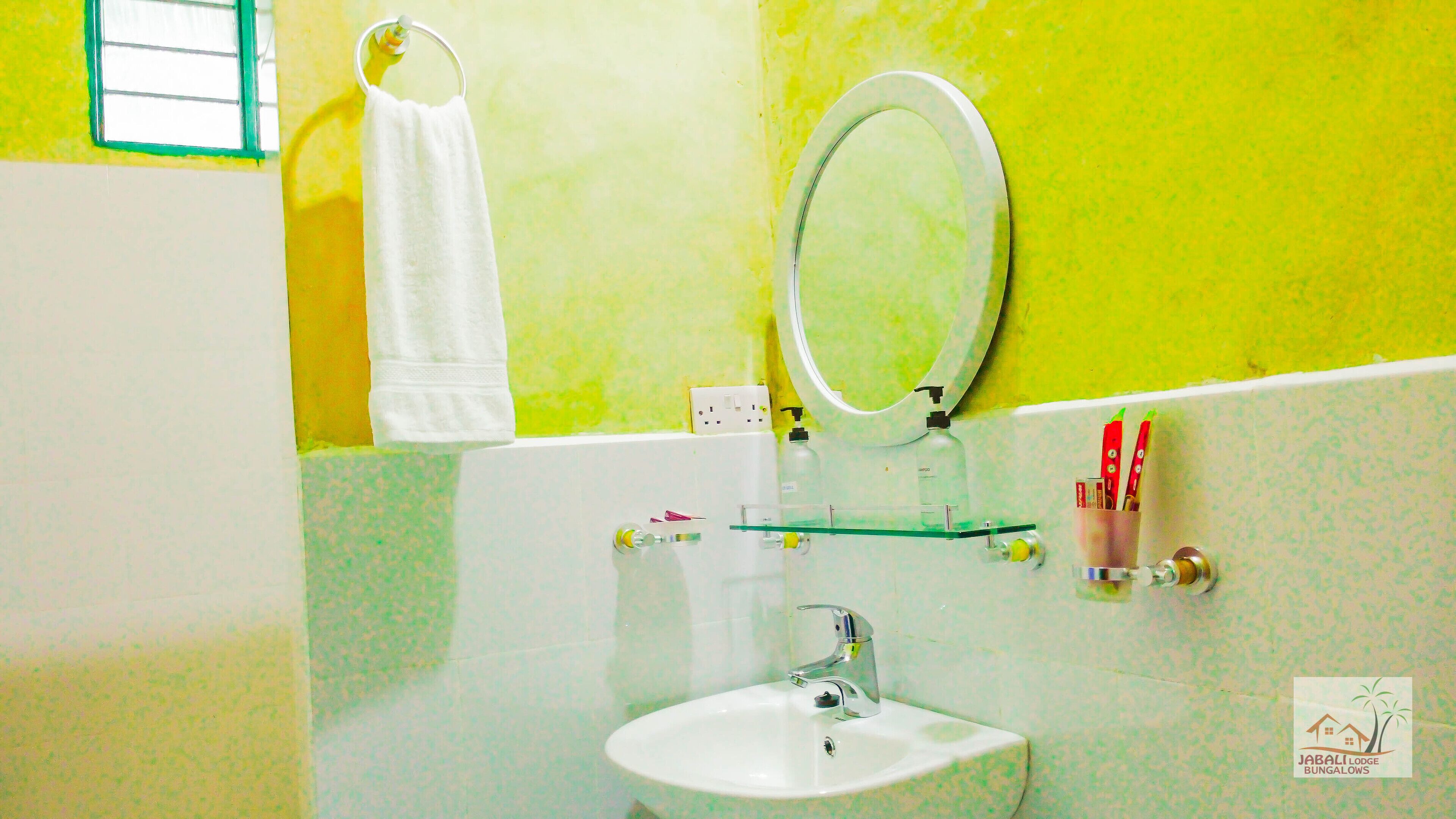 A bathroom with a white sink, a mirror, a glass shelf, and a towel hanging on a ring.