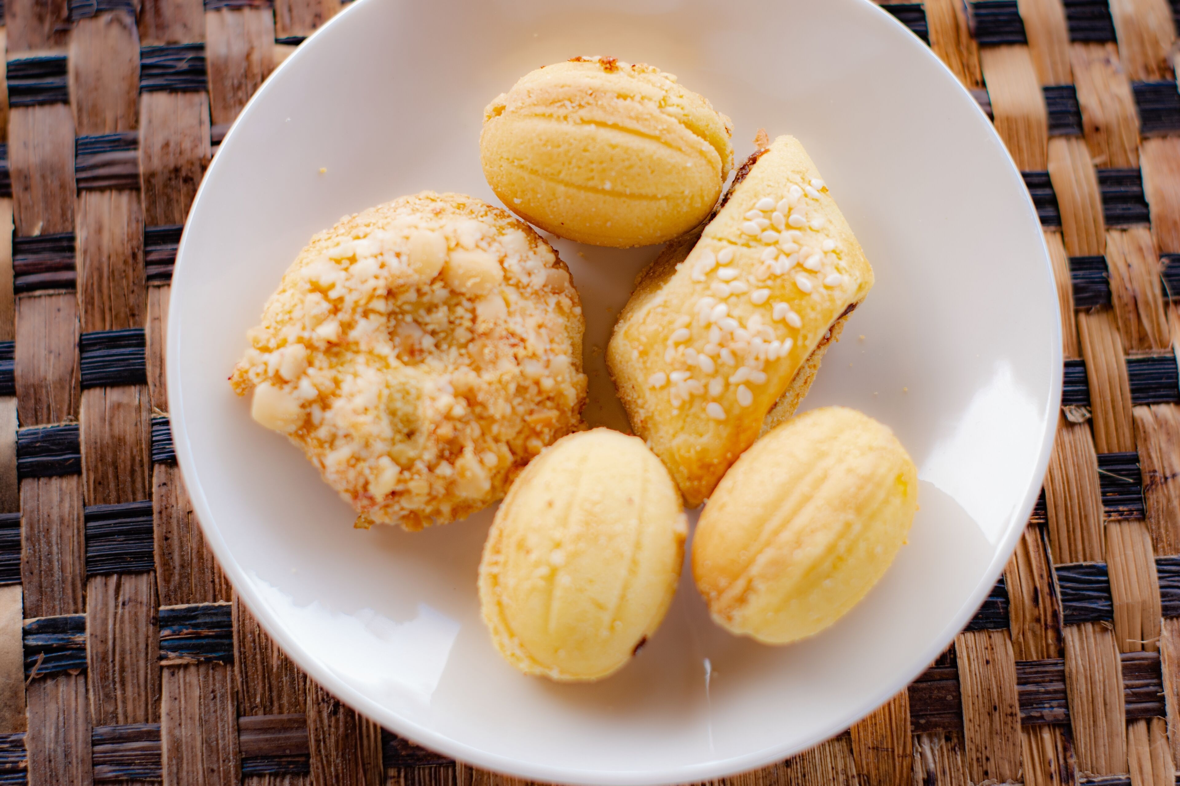 A white plate with five round pastries on a woven surface.