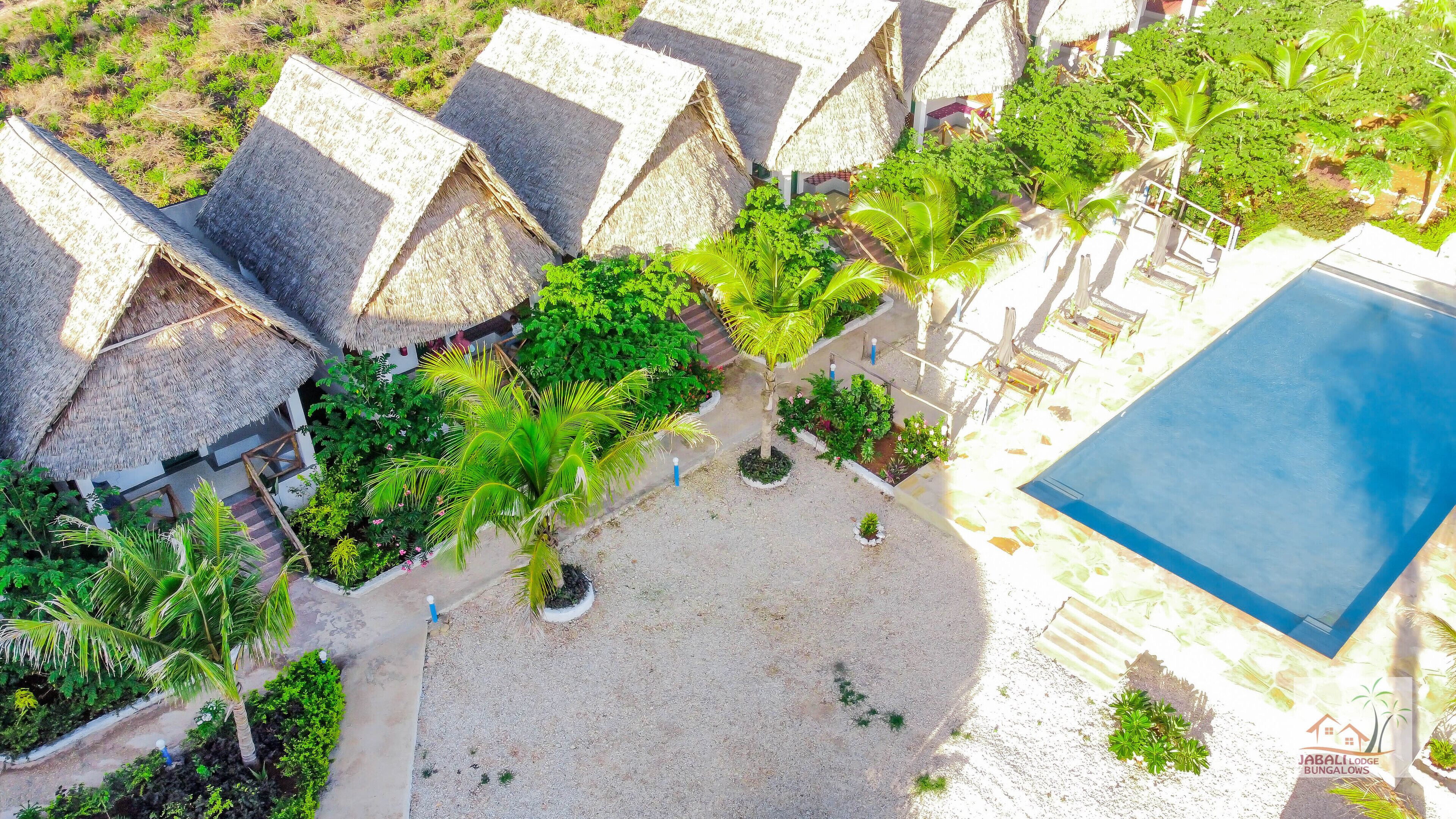 Un resort con bungalows de techo de paja, una piscina y un jardín bien cuidado.