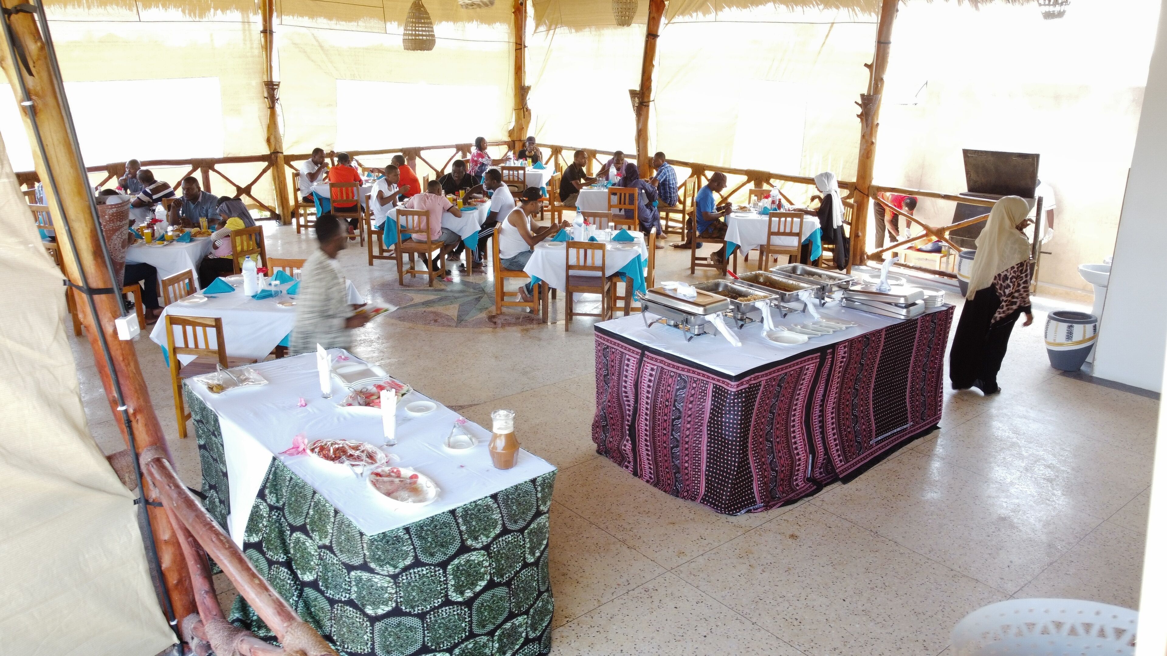 A covered dining area with multiple tables and chairs, a buffet station, and a tiled floor.