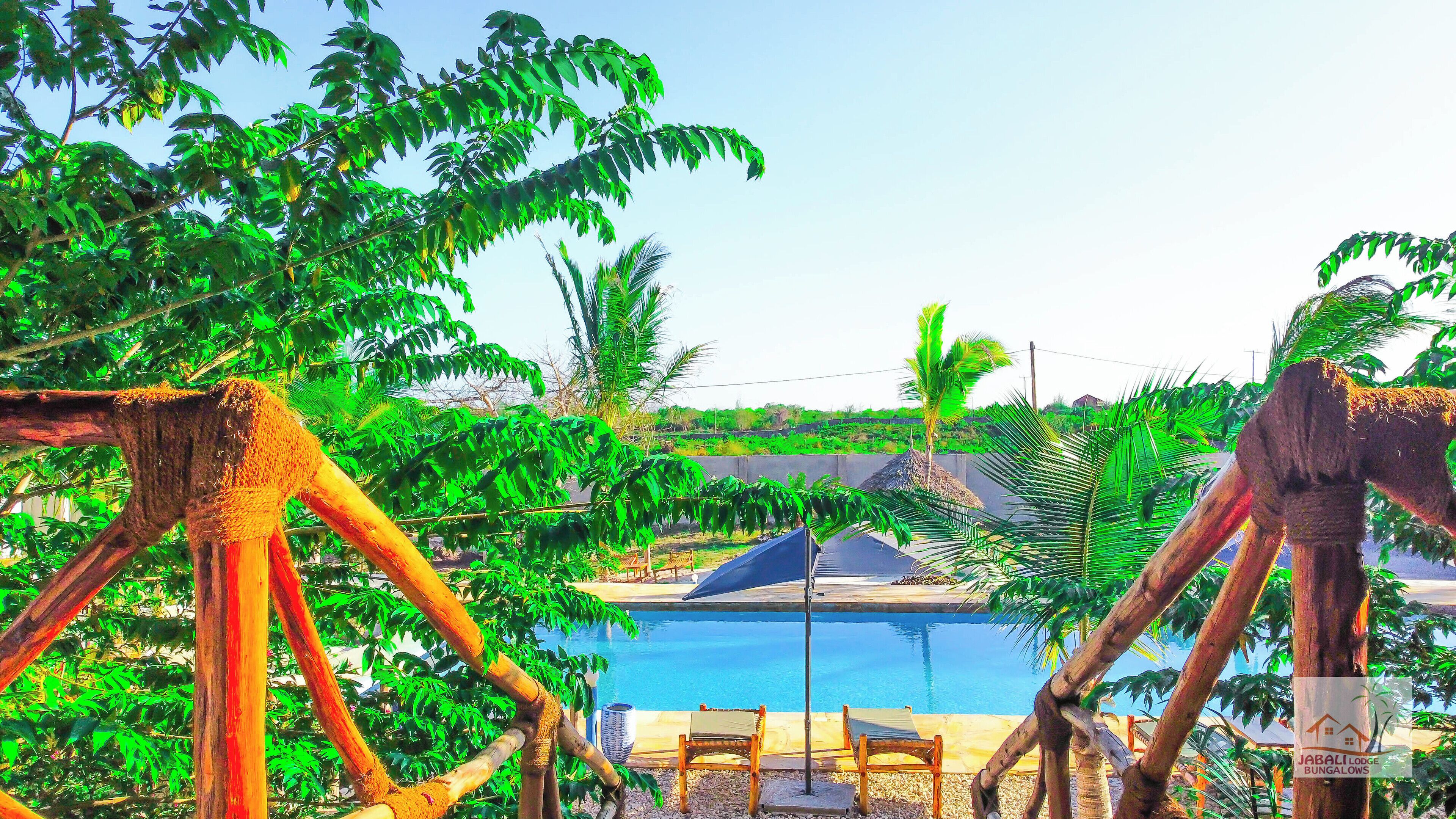 Un espace piscine agrémenté de structures en bois et d’un panneau indiquant « JABALI LODGE BUNGALOWS ».