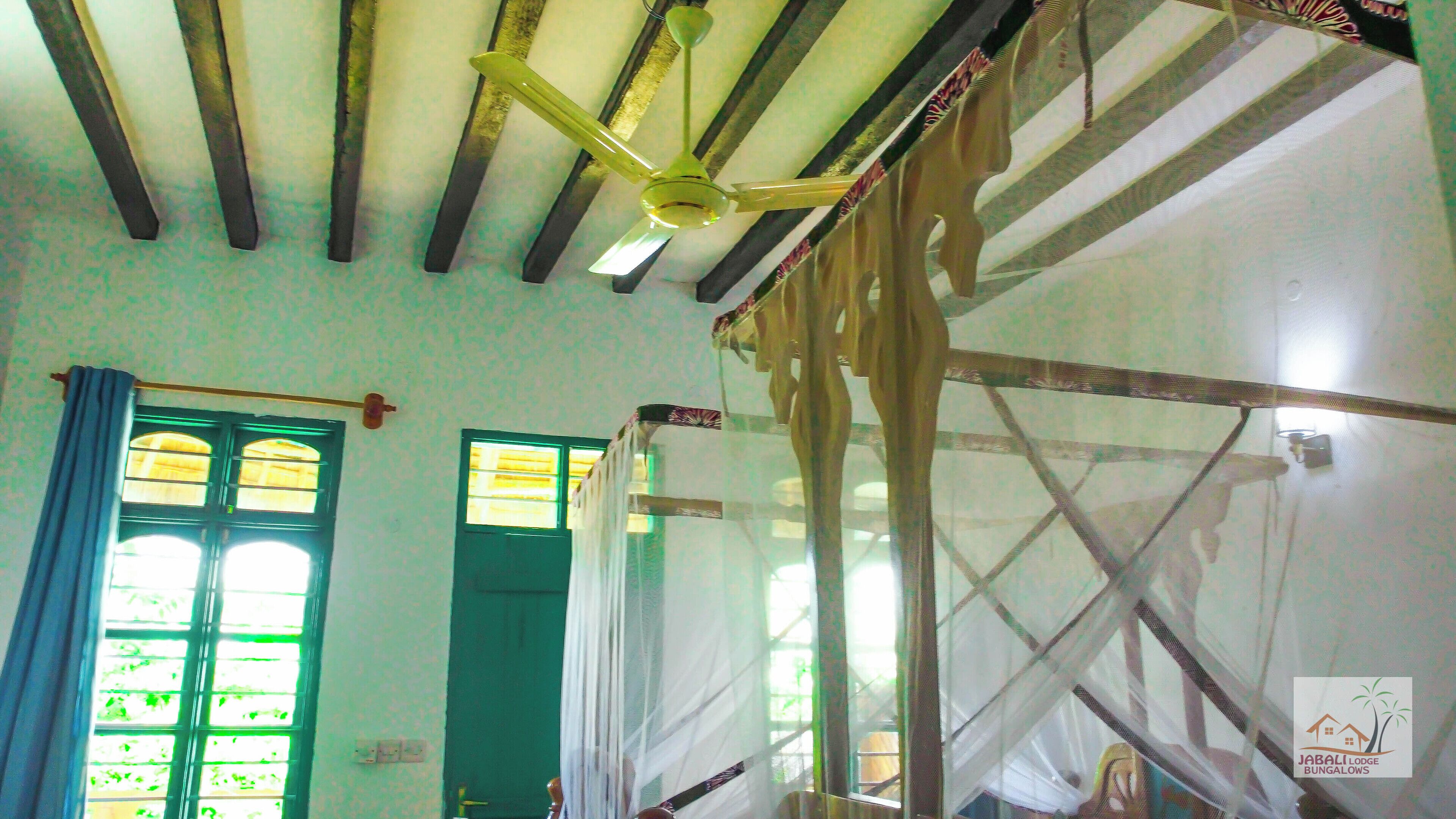 A room with a ceiling fan, a green door, and a window with multiple panes.