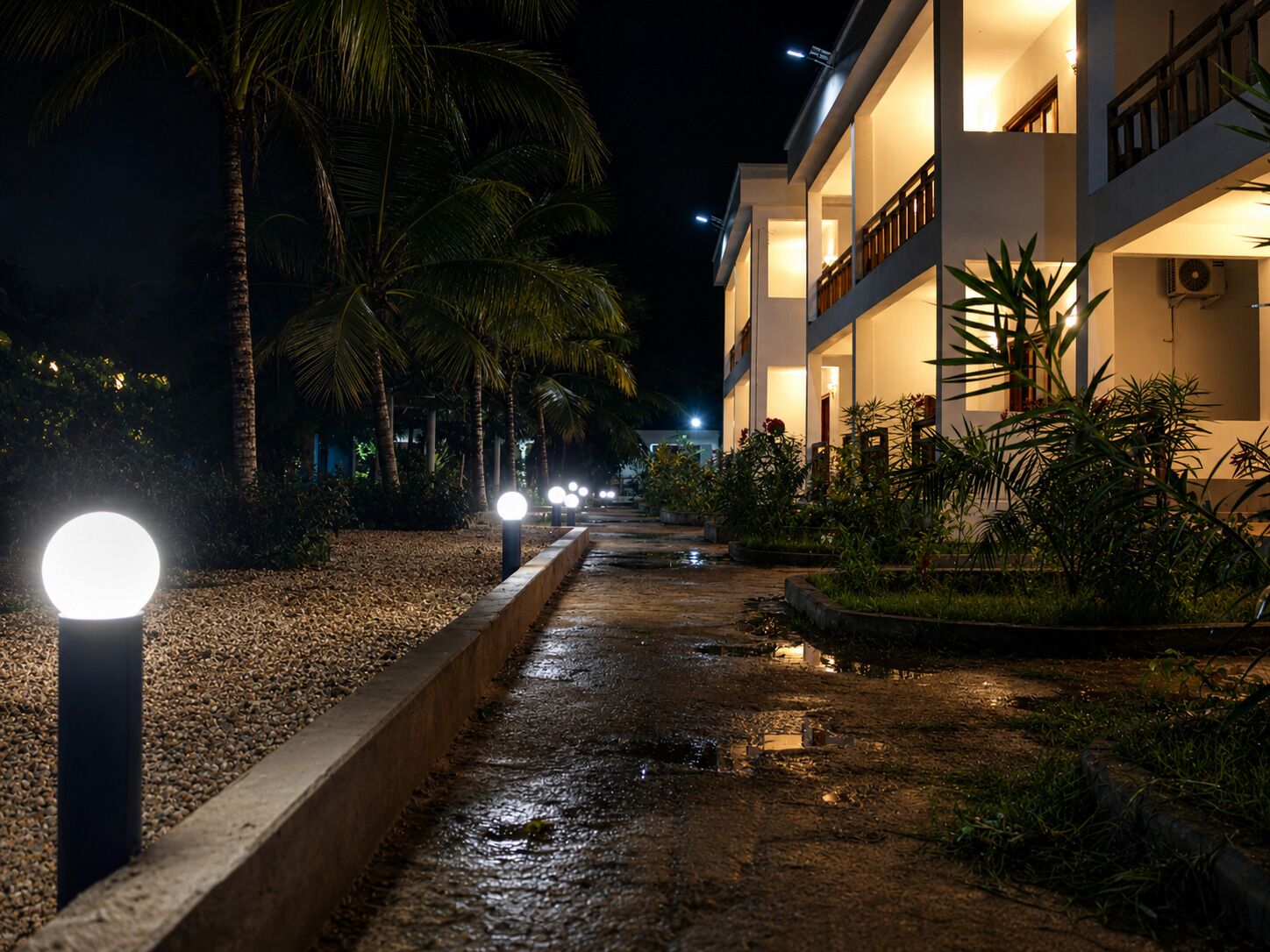 Vista nocturna de un hotel con un camino bordeado de palmeras y una fuente de agua.