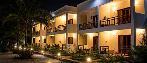 A multi-story hotel with balconies, outdoor lighting, and a gravel pathway.