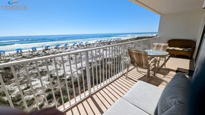 A balcony with a view of the beach, a wicker sofa, a small table, and a chair. - Palms 204 Beachfront Condo with Free Beach Service! (Fort Walton Beach)