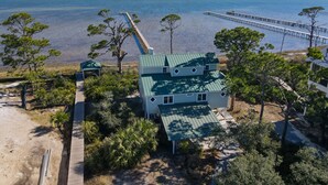 A two-story house with a green roof, surrounded by trees and a dock extending into a body of water. - Bayfront with Gulf and Pool Access (Port Saint Joe)