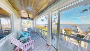 A covered porch with wooden flooring, a ceiling fan, and a view of a beach and bridge. - Bayfront with Gulf and Pool Access (Port Saint Joe)