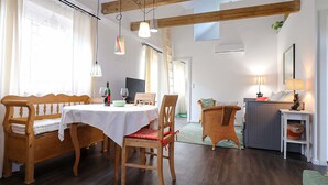 Un coin repas avec une table dressée pour deux personnes, des chaises en bois et un banc. Une bouteille de vin et des verres sont posés sur la table.
