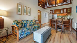 A spacious living area with a wooden ceiling, a dining table with chairs, a sofa with a floral cover, and framed leaf artwork on the wall. - Summer Deal Kona Condo with Private Lanai Pool and Fast WiFi (Kailua Kona)