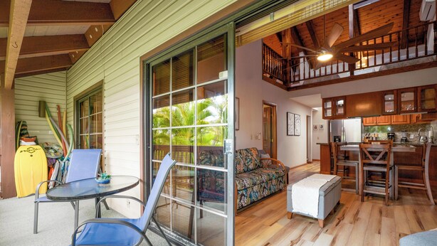 A spacious living area with a sliding glass door leading to a balcony, a dining area with wooden furniture, and a kitchen with wooden cabinets. - Summer Deal Kona Condo with Private Lanai Pool and Fast WiFi (Kailua Kona)