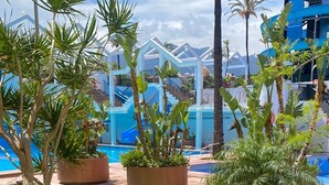 A terrace with white plastic chairs and a small round table, overlooking a pool area with potted plants and a blue building in the background. - Benal Beach resort Benalmadena Malaga pools and slides wifi parking, (Benalmádena)