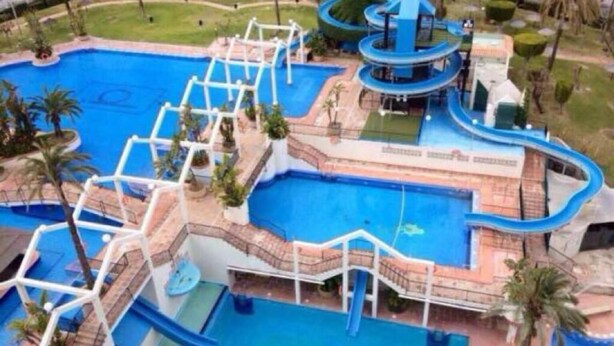 A large outdoor swimming pool with multiple levels and slides, surrounded by palm trees and a small garden area. - Benal Beach resort Benalmadena Malaga pools and slides wifi parking, (Benalmádena)