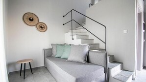 A modern living space with a grey sofa, a small wooden stool, and a staircase with a metal railing. - HERACLEA SUITES (Nea Propontida)