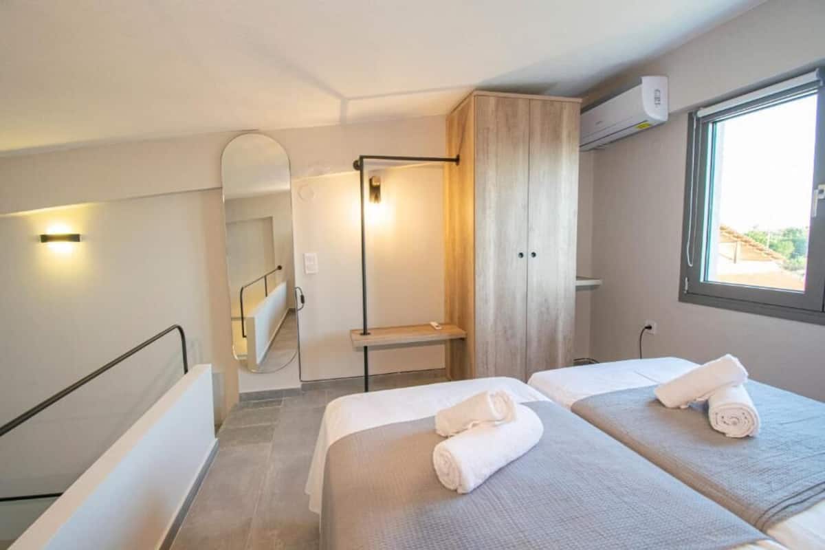 Une chambre d’hôtel avec deux lits, un espace douche et une fenêtre laissant entrer la lumière naturelle.