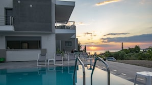A modern building with a swimming pool, outdoor seating, and a sunset view. - HERACLEA SUITES (Nea Propontida)