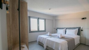 A hotel room with two beds, a wooden wardrobe, a large window, and a ceiling light. - HERACLEA SUITES (Nea Propontida)