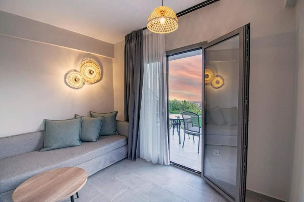 Un salon moderne avec un canapé gris, une table basse en bois et une porte en verre donnant sur un espace extérieur aménagé avec une table et des chaises.