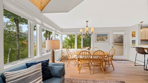A bright dining area with a wooden table and chairs, large windows offering a view of trees, and a chandelier. - Beautiful 2br/2ba Fall Line Condo W/ Mountain Views, Pool, Hot Tub, Sauna, Shuttle. G6b 2 Bedroom Condo (Killington)
