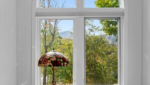 A room with a stained glass lamp on a wooden table, large windows with a view of trees and mountains. - Beautiful 2br/2ba Fall Line Condo W/ Mountain Views, Pool, Hot Tub, Sauna, Shuttle. G6b 2 Bedroom Condo (Killington)