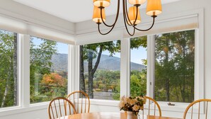 A dining room with a large table and chairs, a vase with flowers, and a view of trees and mountains through large windows. - Beautiful 2br/2ba Fall Line Condo W/ Mountain Views, Pool, Hot Tub, Sauna, Shuttle. G6b 2 Bedroom Condo (Killington)