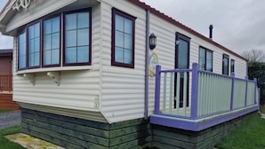 A mobile home with a porch, large windows, and a small deck. - Caravan - Sleeps 4 - Pet Friendly - Parking (Newton Stewart)