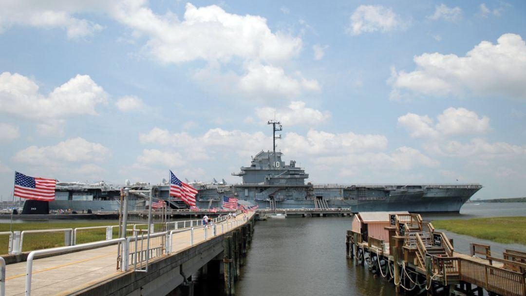 An aircraft carrier docked at a pier with American flags and a wooden walkway.